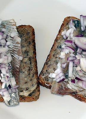 Twee sneetjes brood met haring en uitjes erop.