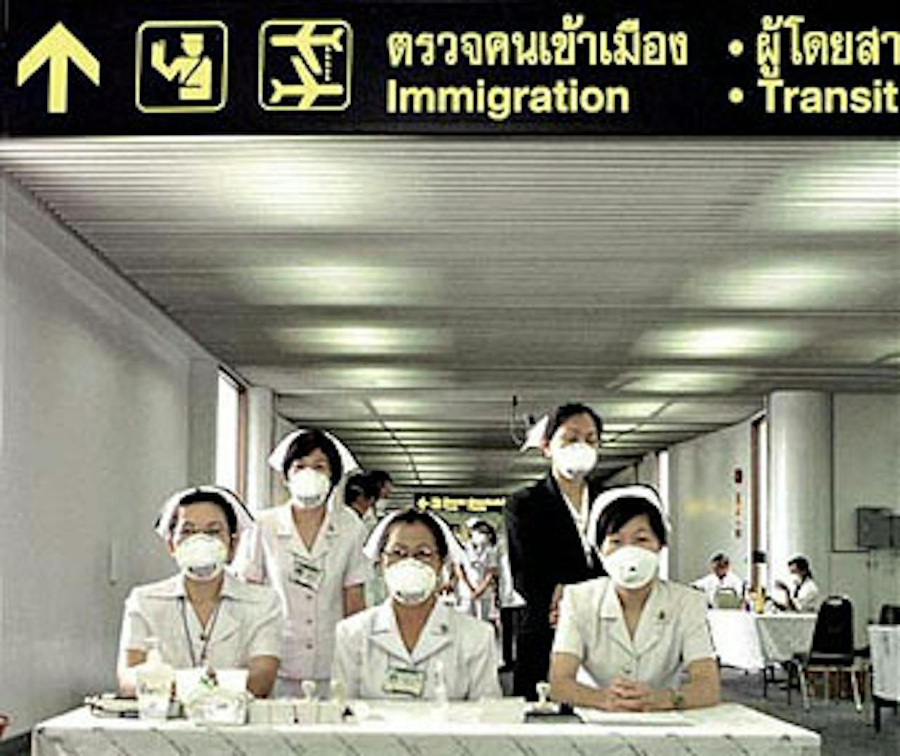 Vijf personen lopen op een luchthaven met witte mondkapjes op.