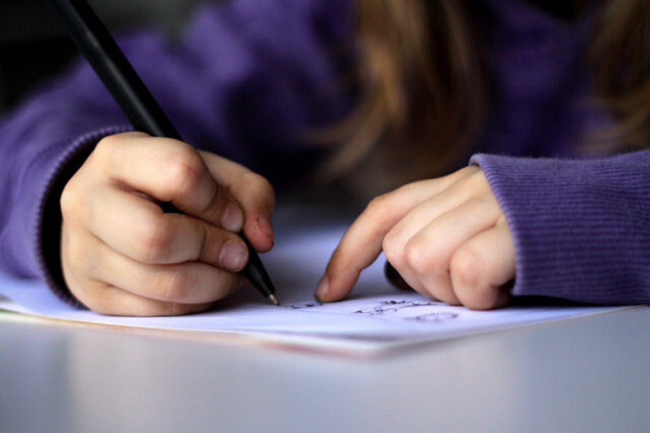 Een kind schrfijt met een pen op een stuk papier.