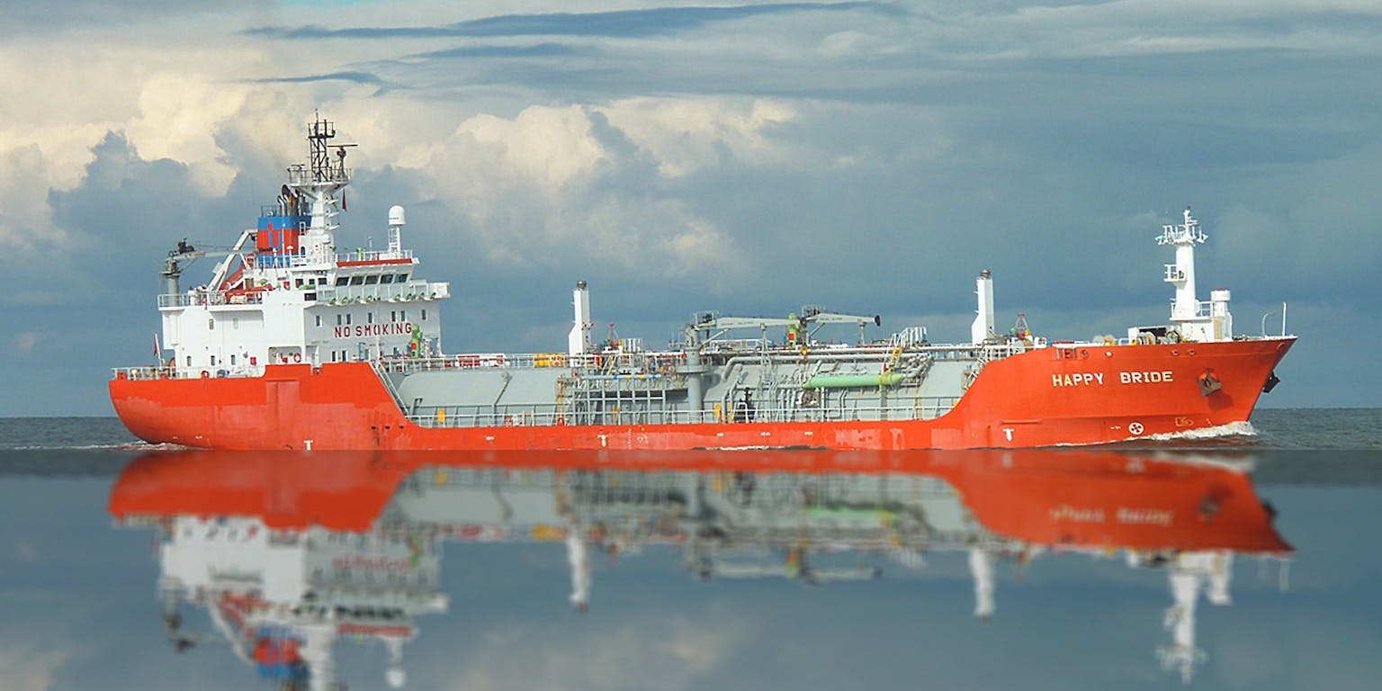 Een oranje olietanker van de zijkant bezien weerspiegelt in het strakke wateroppervlak.