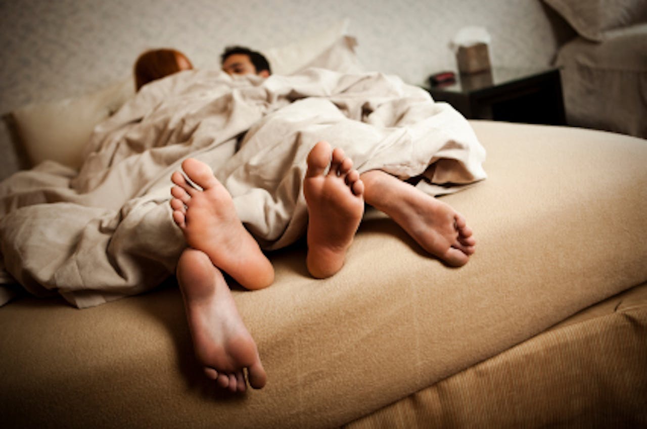 Twee personen liggen samen op bed onder het dekbed. Allebei hebben ze blote voeten.