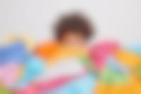 gezicht van jonge vrouw gaat schuil achter een enorme berg met kleding