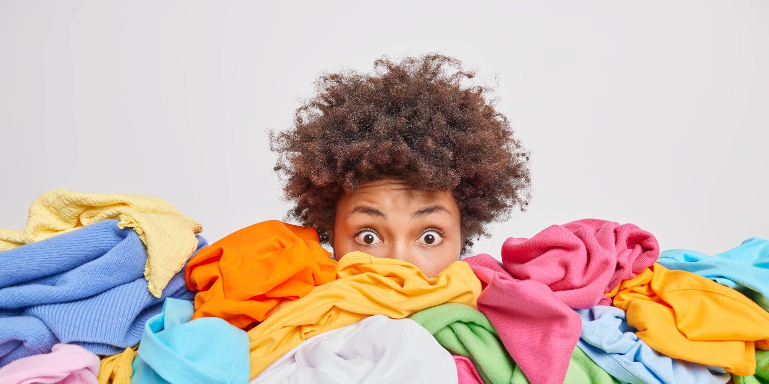 gezicht van jonge vrouw gaat schuil achter een enorme berg met kleding