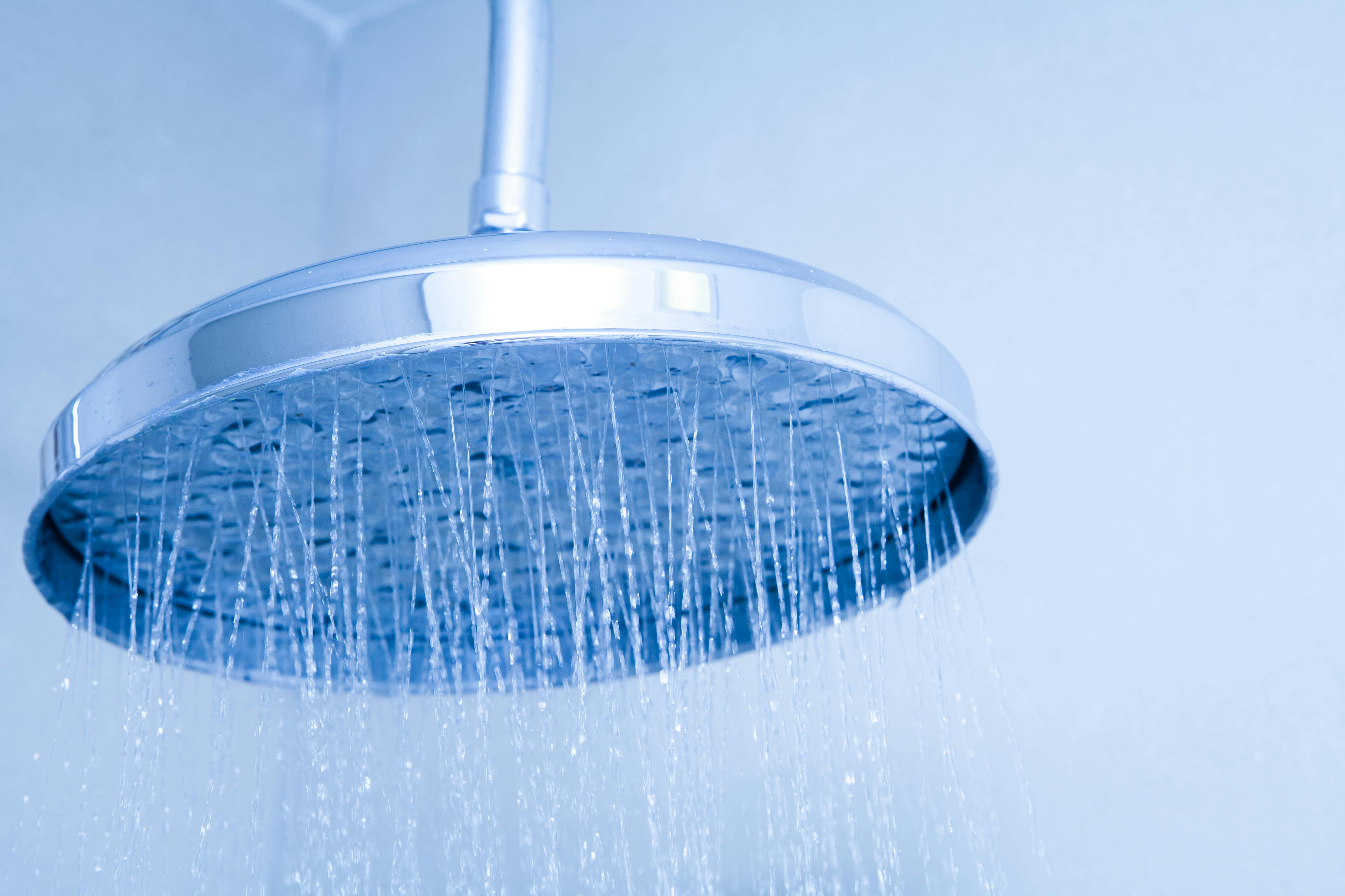 Ingezoomde douchekop waar waterstraaltjes uit komen. De foto is blauw van tint.
