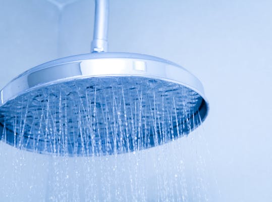 Ingezoomde douchekop waar waterstraaltjes uit komen. De foto is blauw van tint.