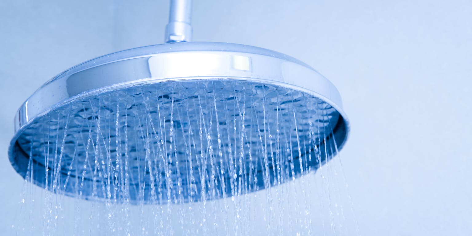 Ingezoomde douchekop waar waterstraaltjes uit komen. De foto is blauw van tint.