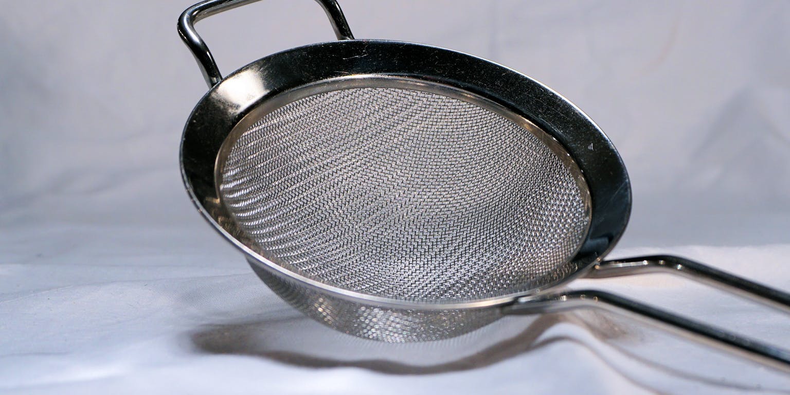 Een metalen zeef met een handvat op een wit oppervlak.