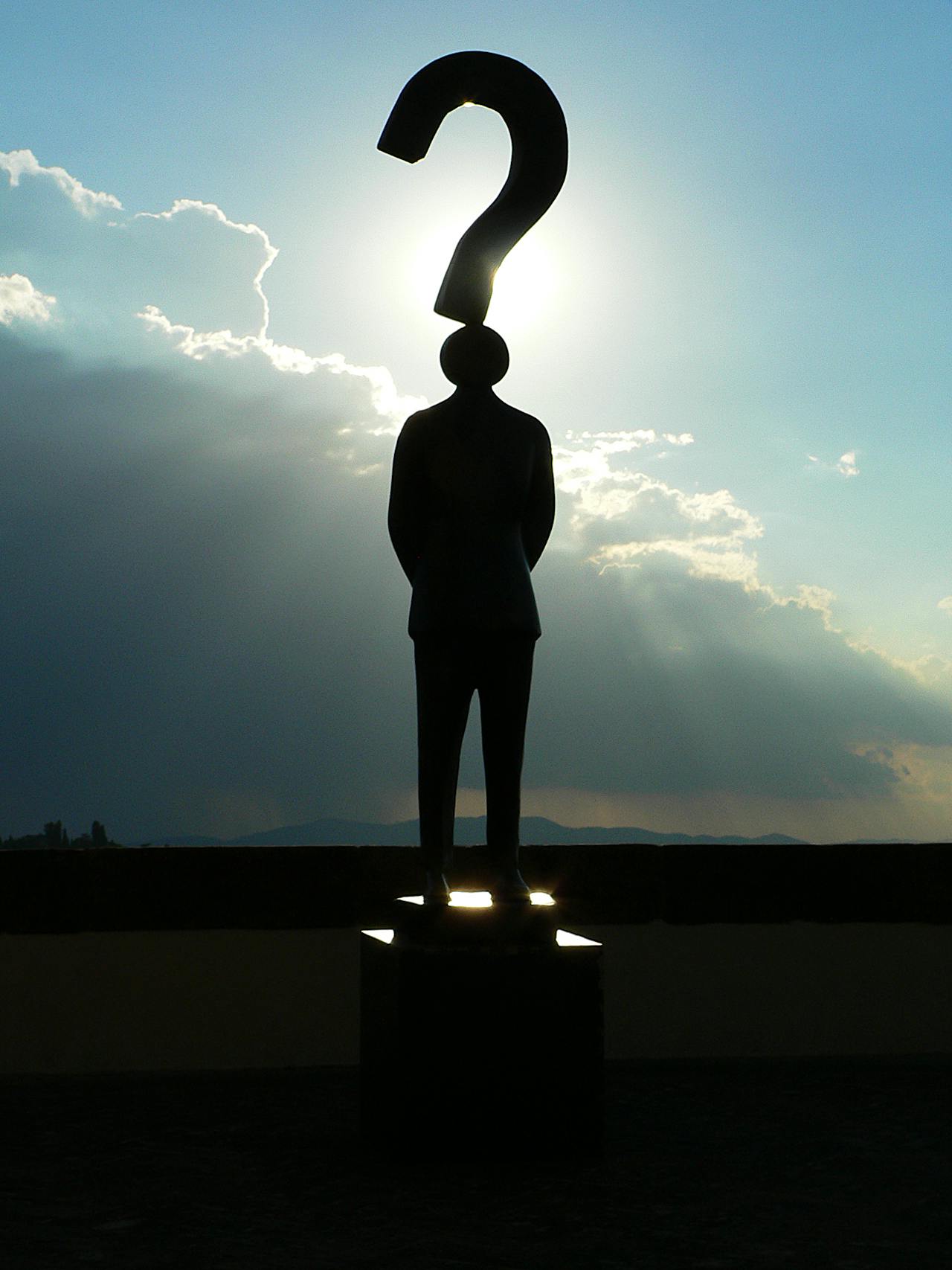 Een silhouette van een persoon met een vraagteken boven het hoofd. Er zijn wolken op de achtergrond.