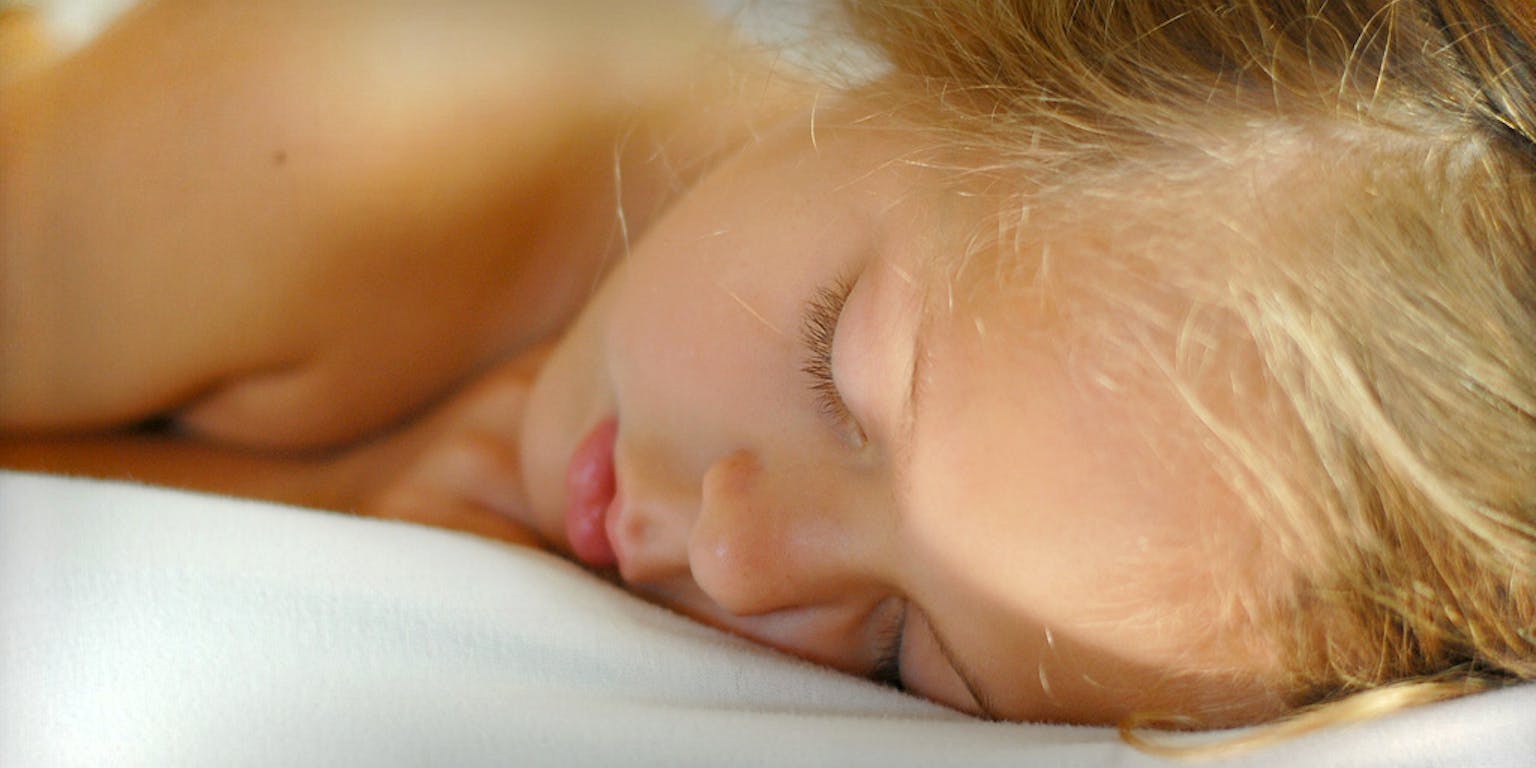 Een jong meisje slaapt op een bed.