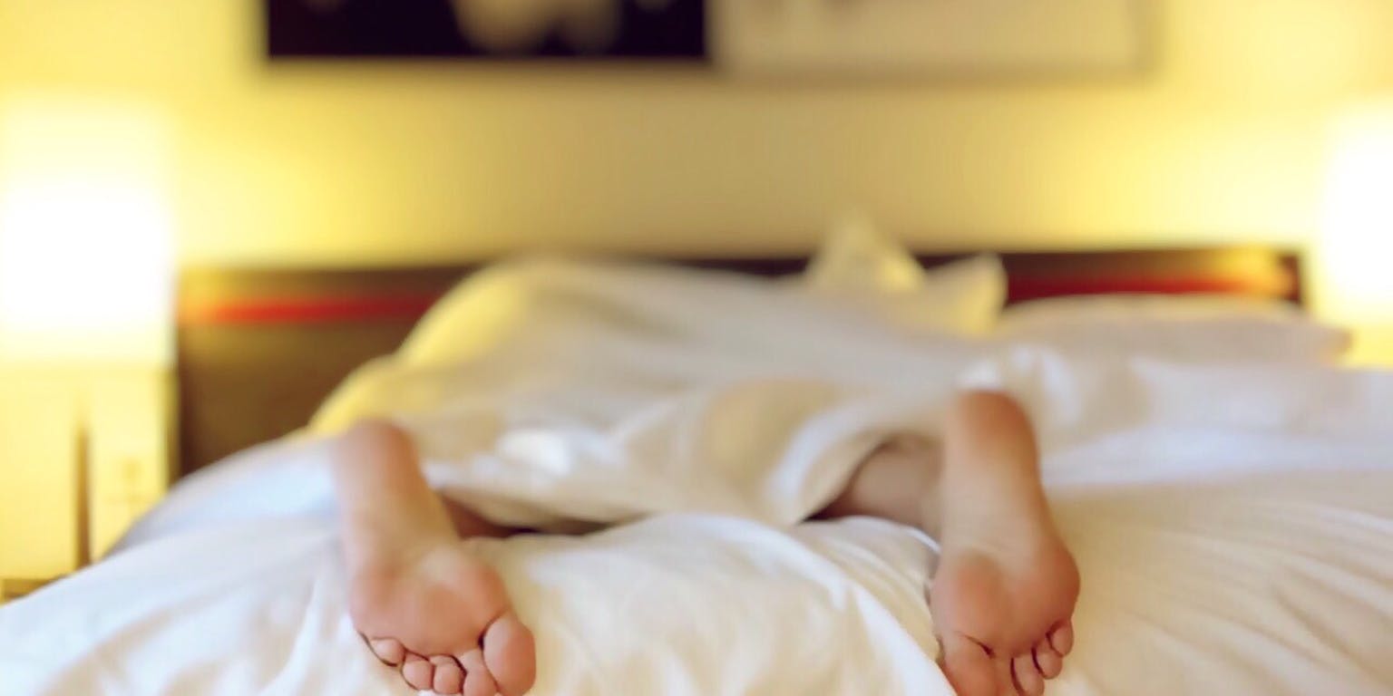 De voeten van een persoon liggen op een bed met witte lakens.