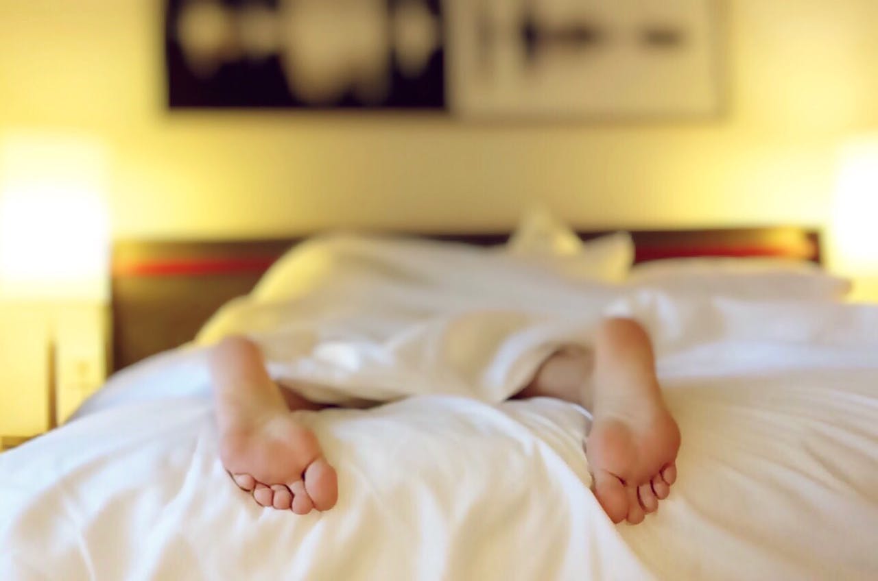 De voeten van een persoon liggen op een bed met witte lakens.