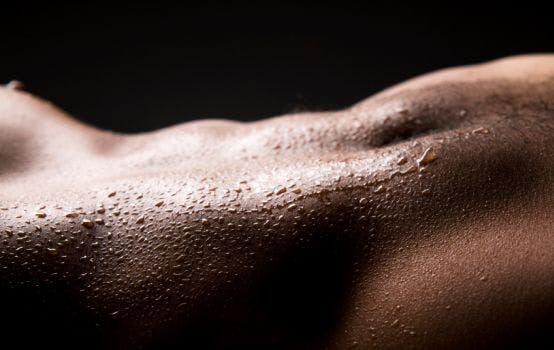 Het torso van een man met zweetdruppels erop.