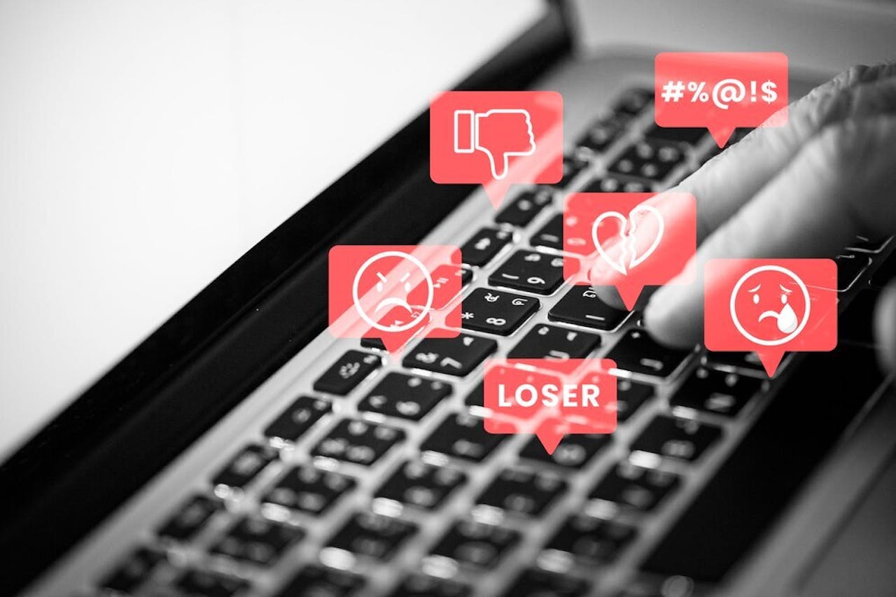 toetsenbord met online haatberichten in rode tekstballonnetjes zoals loser, een huilende smiley en een duimpje naar beneden