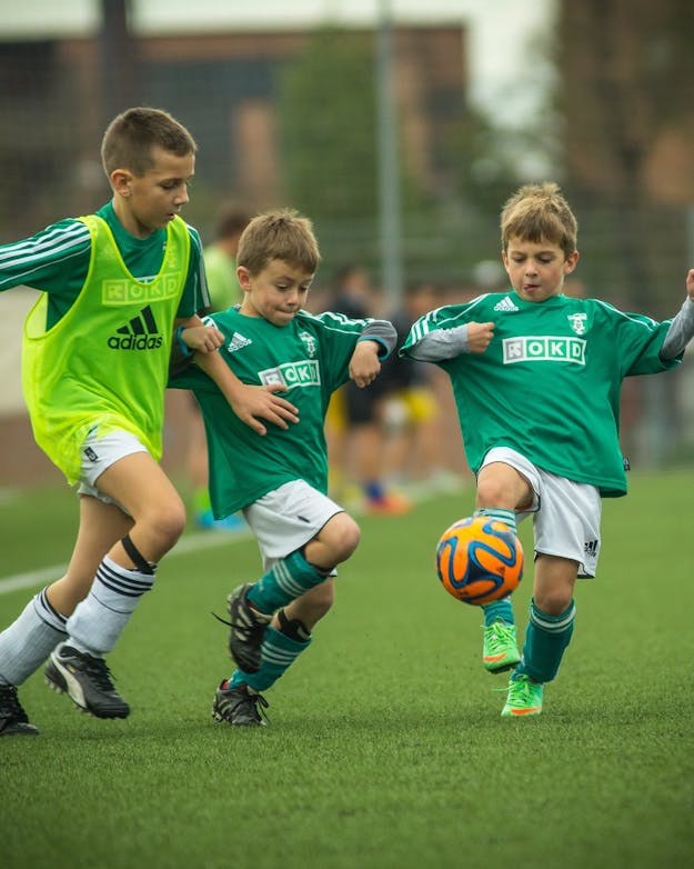 Tijdens een voetbalwedstrijd zijn drie jongens met elkaar in duel om de bal. Tijdens een voetbalwedstrijd zijn drie jongens met elkaar in duel om de bal.