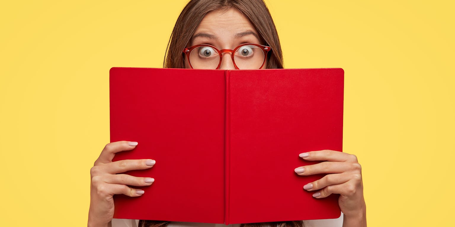 Een jonge vrouw met bril leest geschokt in een rood boek