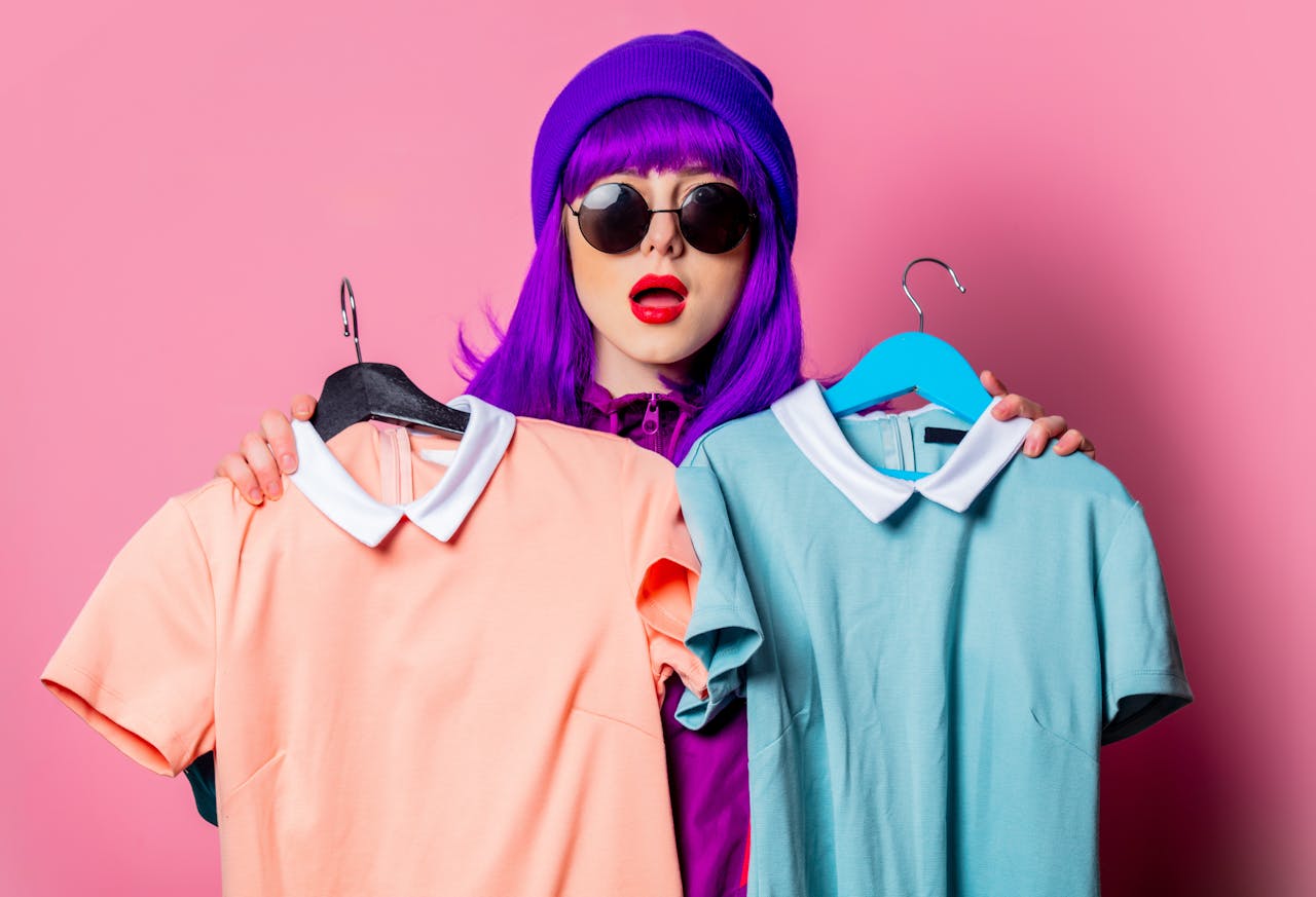 In de toekomst scan je misschien de QR-code op het label om exact te weten wat de impact is van je potentiële nieuwe kledingstuk op het milieu. jonge vrouw met paars haar en zonnebril houdt twee kleurrijke shirts vast