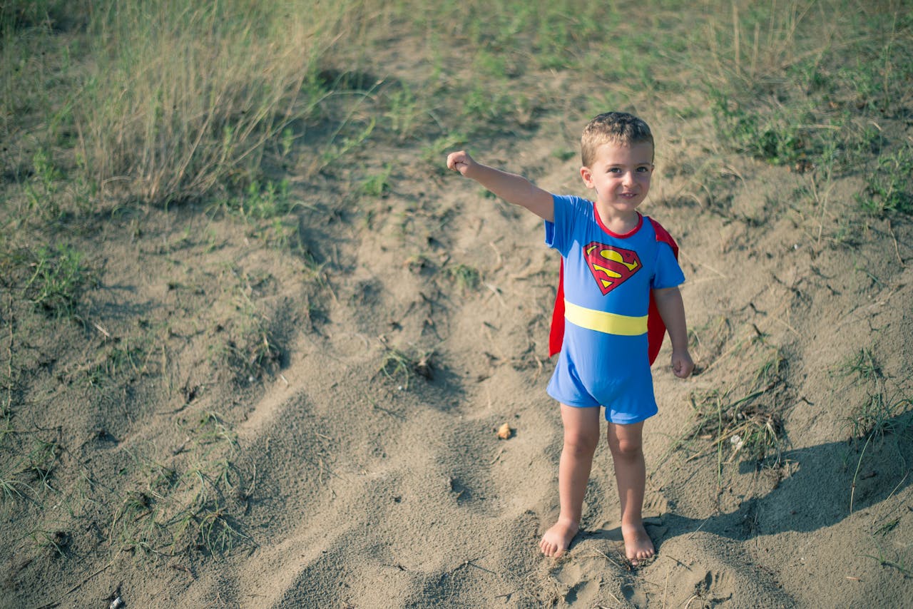 Een jonge jongen in een supermankostuum dat in het zand staat.