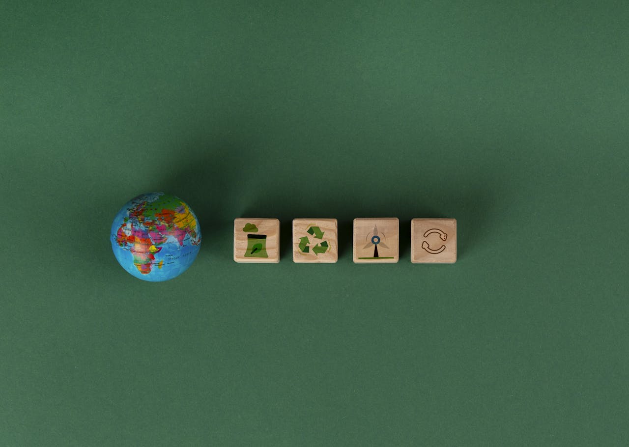 kleine wereldbol op groene achtergrond met houten blokjes die duurzaamheid symboliseren, zoals recycleteken en windenergie