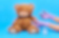 Een teddybeer krijgt een spuitje van iemand met handschoenen aan en witte doktersjas aan