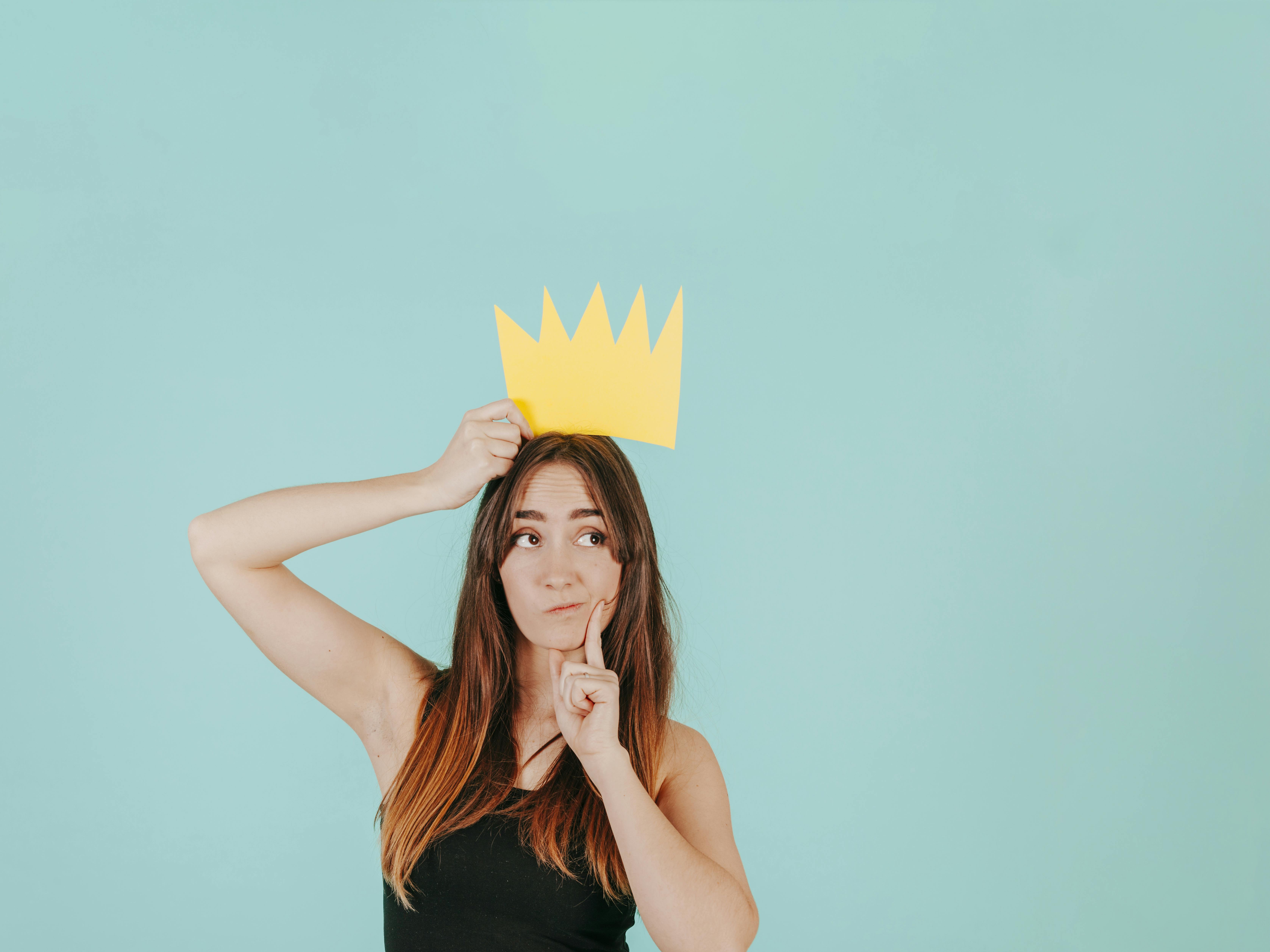 Jonge vrouw houdt papieren kroon boven haar hoofd vast en twijfelt of zij wel de winnaar is, of de verliezer