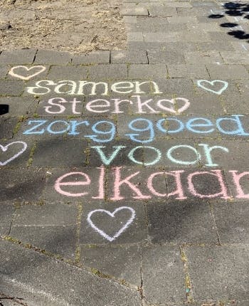 Op straat is met stoepkrijt het volgende geschreven: samen sterk. Zorg goed voor elkaar. Er zijn hartjes bij getekend.