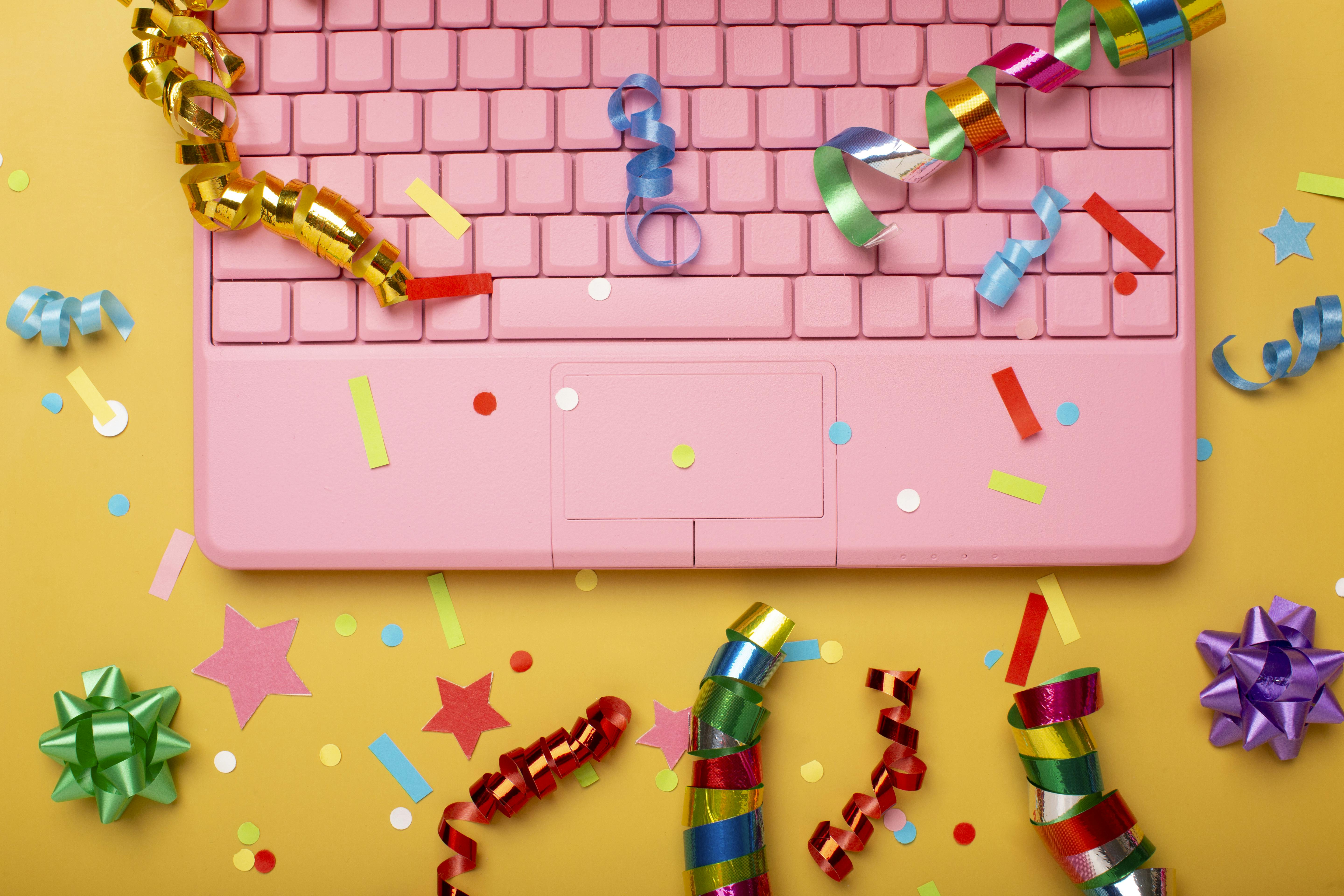 roze laptop met kleurige feestartikelen eromheen