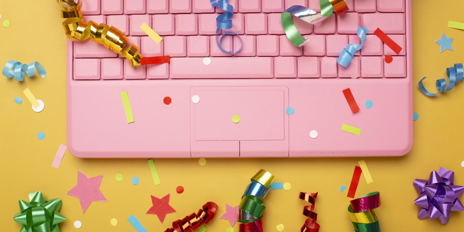 roze laptop met kleurige feestartikelen eromheen