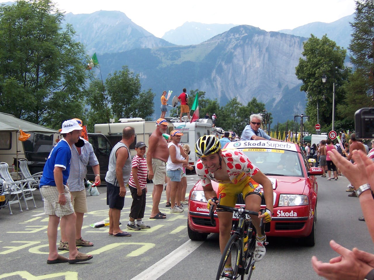Een man rijdt op een fiets de Tour de France. Er staan mensen langs de zijlijn.