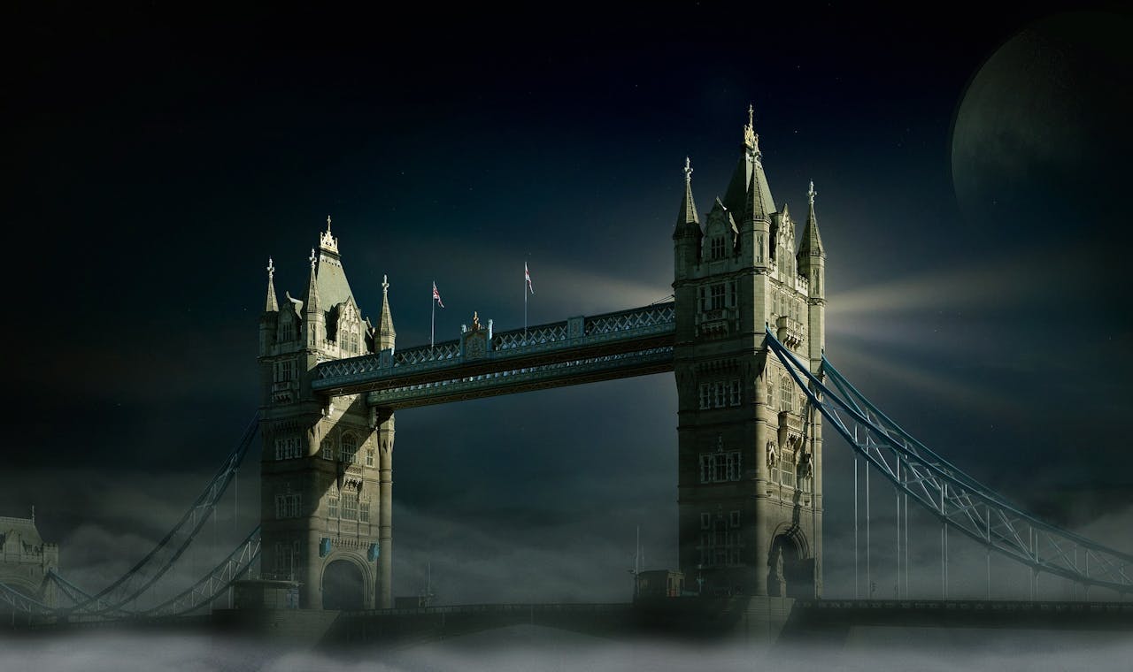 Een foto van de Tower Bridge in London. Het is donker, mistig en de maan is zichtbaar.