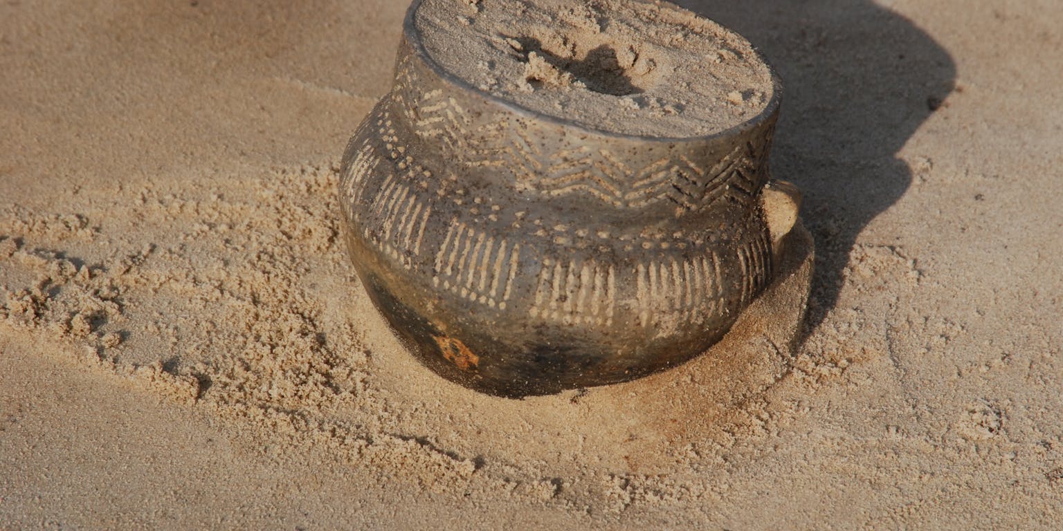 Versierde trechterbeker als grafgift in het zand.