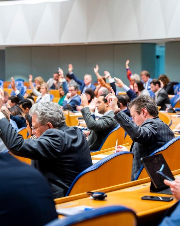 Een stemming in de Tweede Kamer Leden van de Tweede Kamer stemmen over een motie. De leden zijn schuin op de rug gefotograffeerd.
