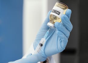 Een hand met een blauwe handschoen die een vaccin in een spuitje spuit.