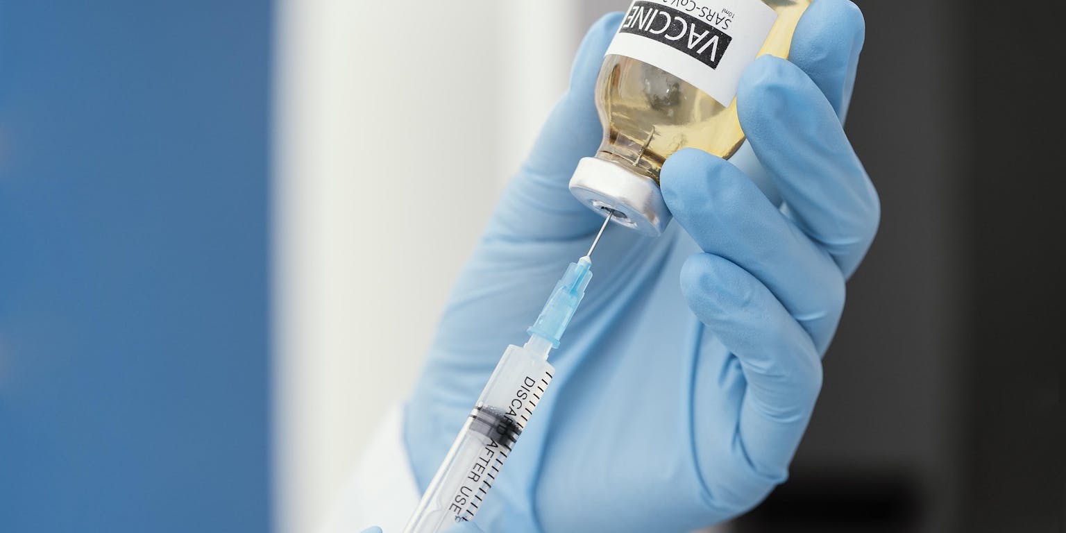 Een hand met een blauwe handschoen die een vaccin in een spuitje spuit.