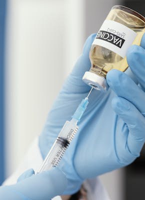 Een hand met een blauwe handschoen die een vaccin in een spuitje spuit.