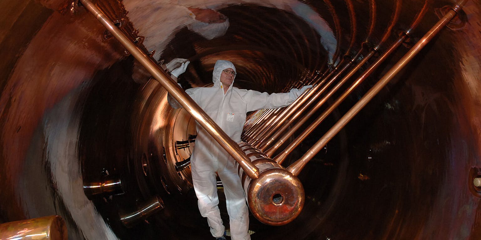 Een man in een wit pak staat in een deeltjesversneller.