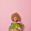 jonge vrouw met springerig haar die heel veel verschillende groenten vasthoudt en blij kijkt