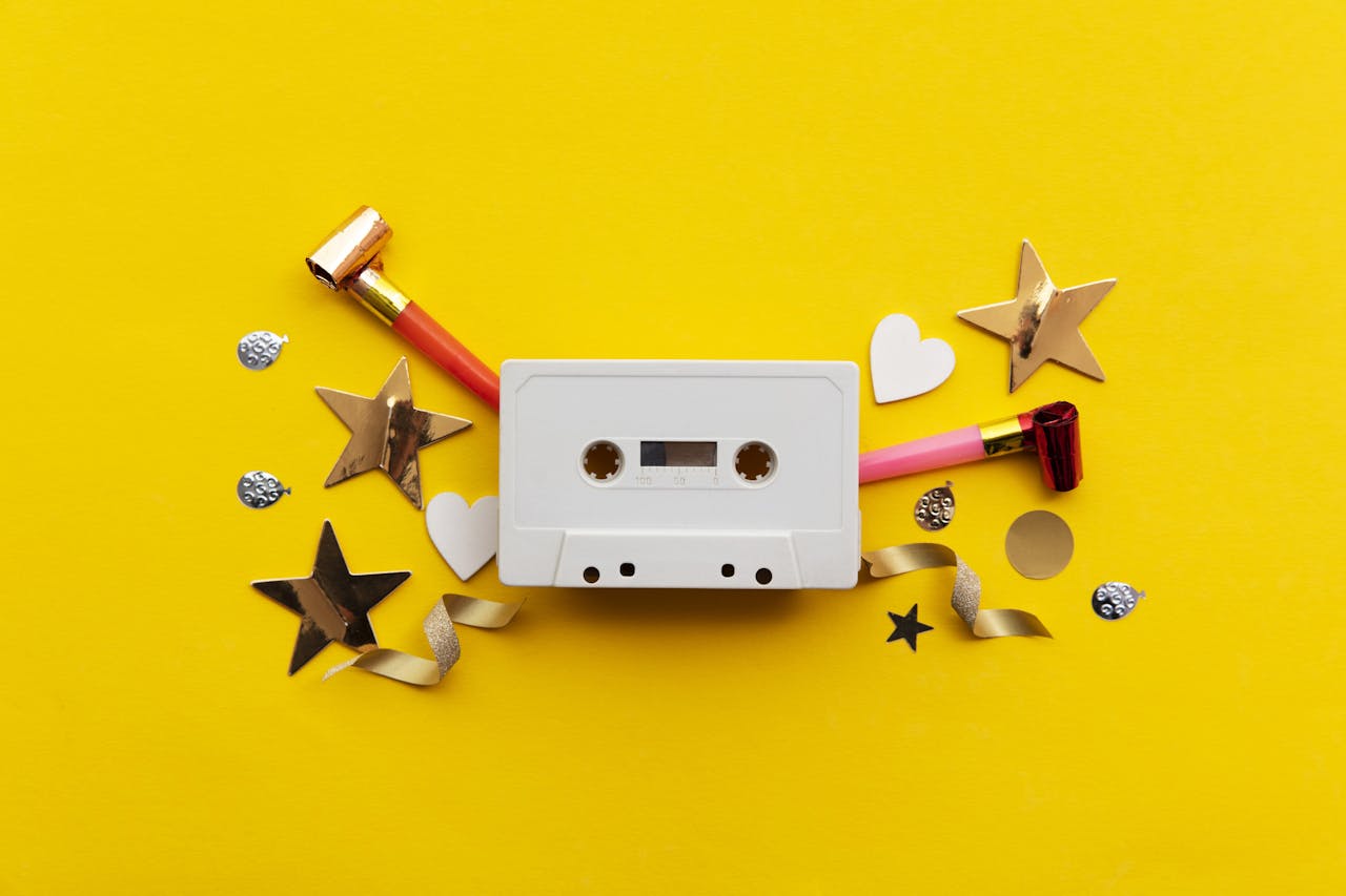 cassettebandje met feestartikelen zoals een roltoeter en glitters tegen een gele achtergrond