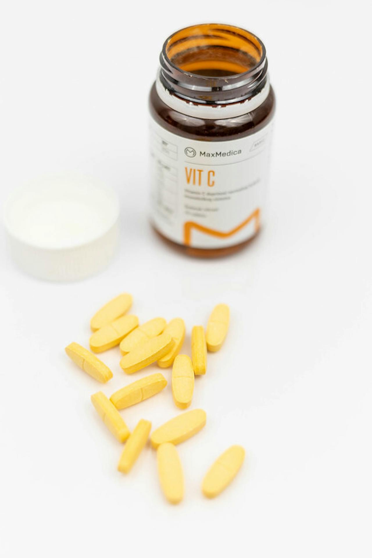 Gele vitamine C-capsules naast een pot op een wit oppervlak.