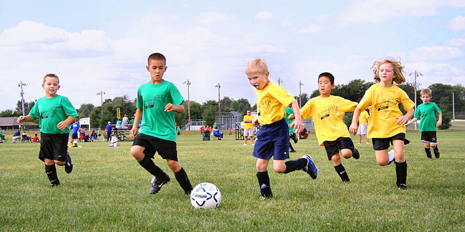 Een groep kinderen voetballen op een veld.