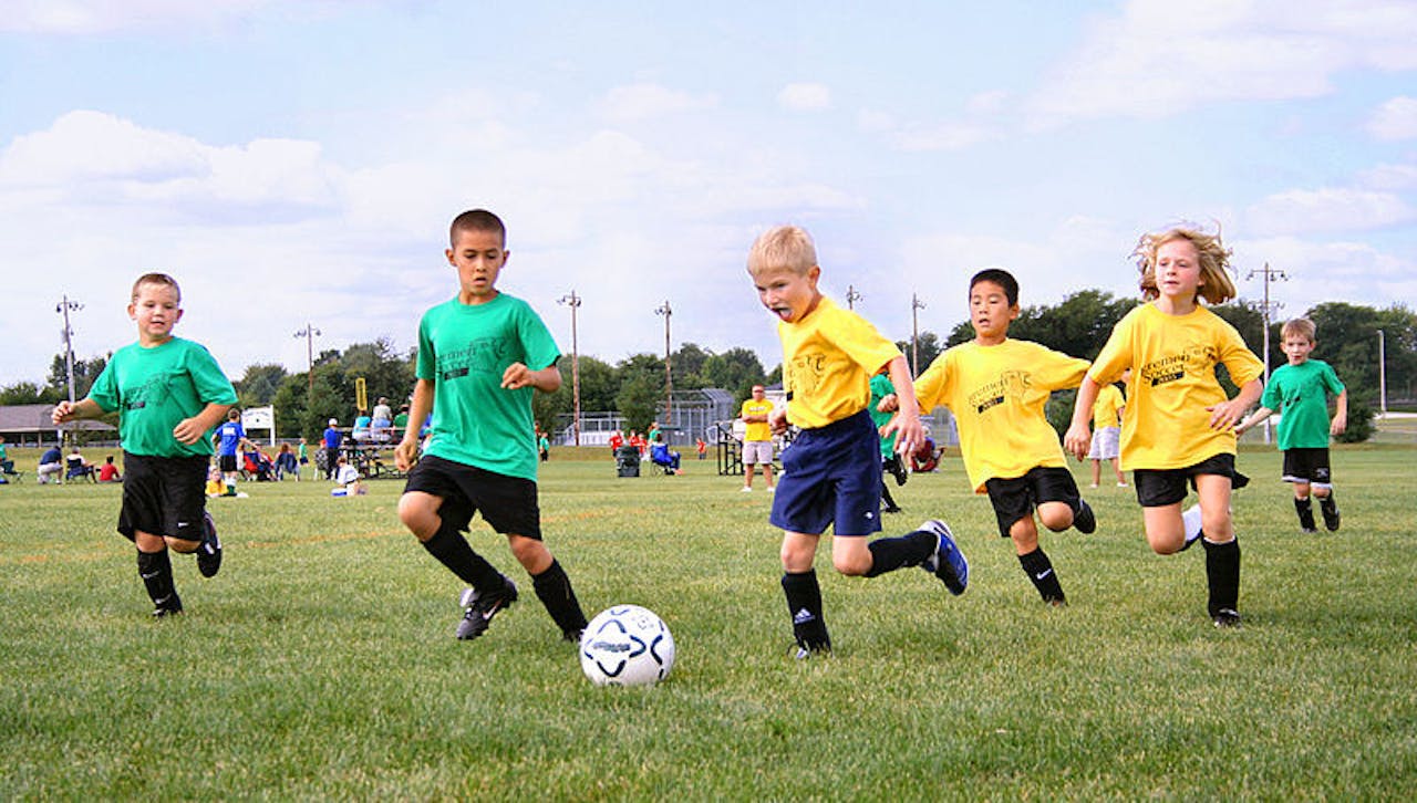 Een groep kinderen voetballen op een veld.