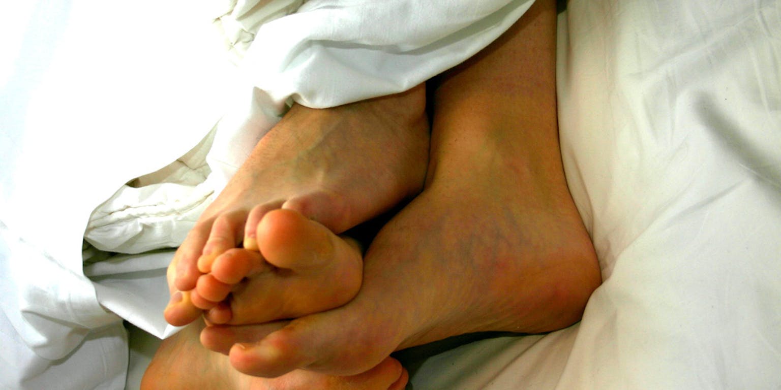 De blote voeten van twee personen onder een wit dekbed.