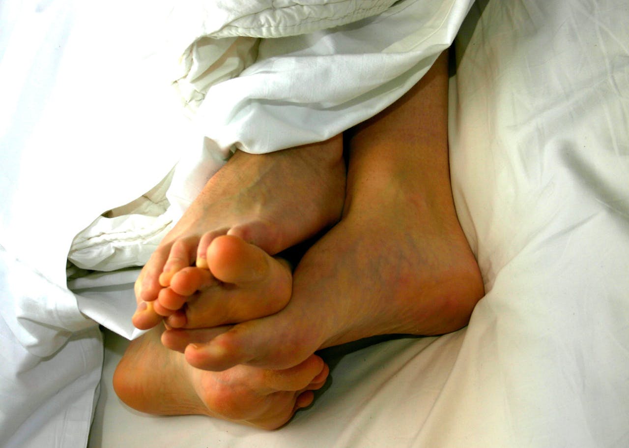 De blote voeten van twee personen onder een wit dekbed.