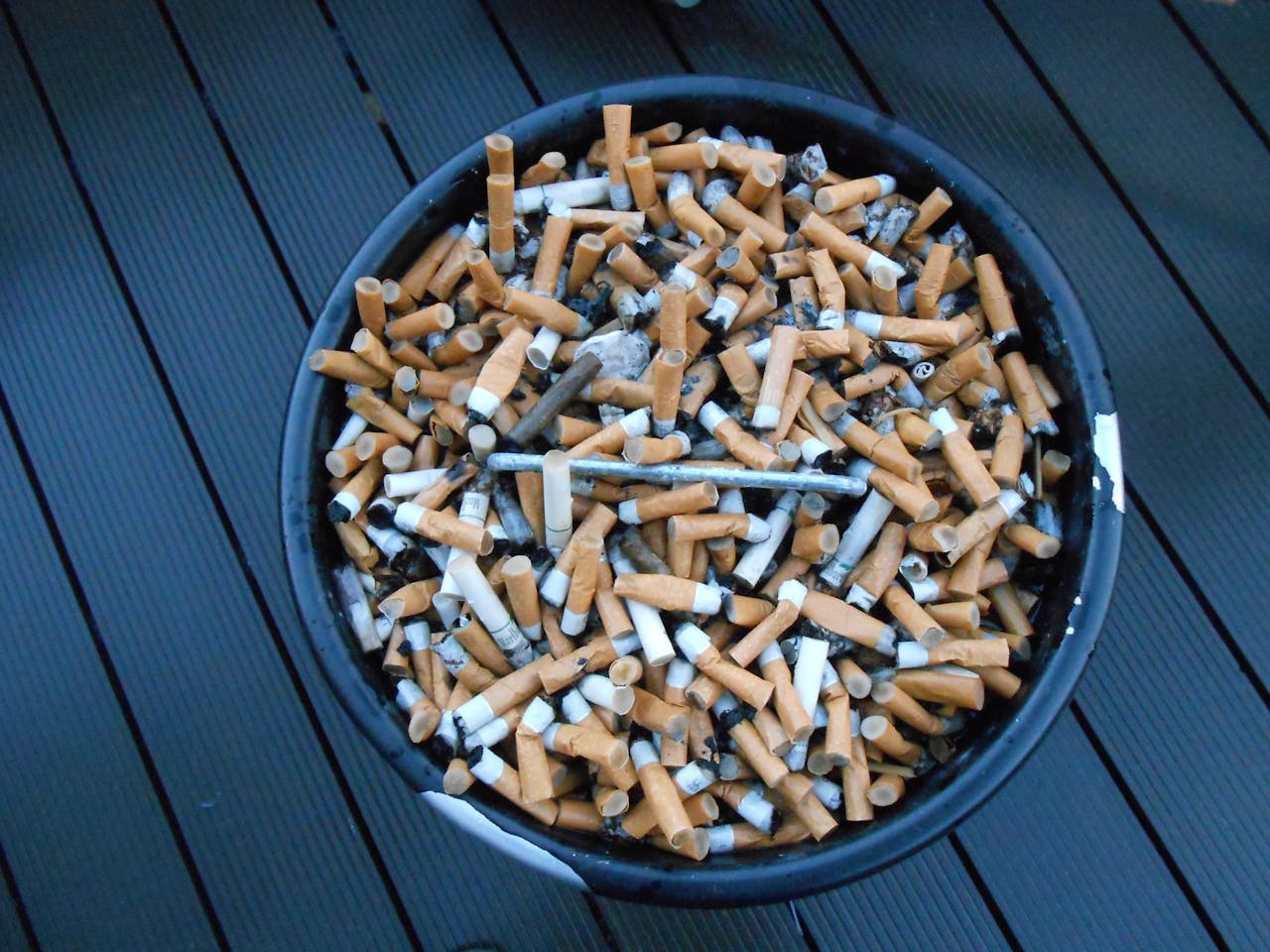 Een emmer vol sigaretten op een houten dek.