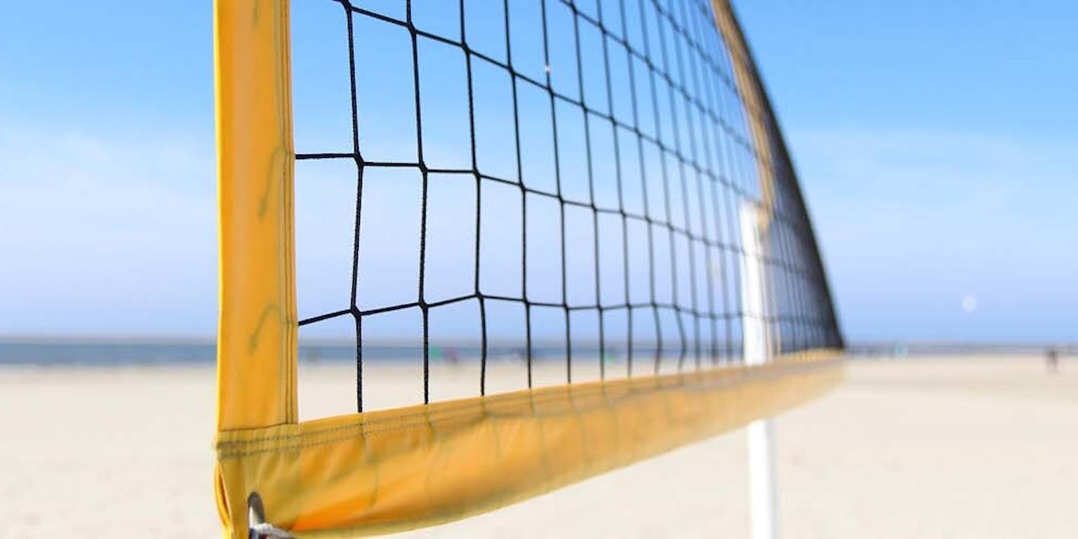 Een close-up van een volleybalnet op het strand met een blauwe lucht.