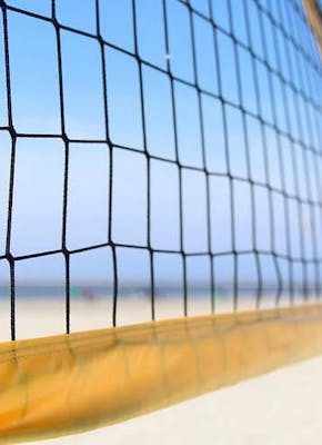 Een close-up van een volleybalnet op het strand met een blauwe lucht.