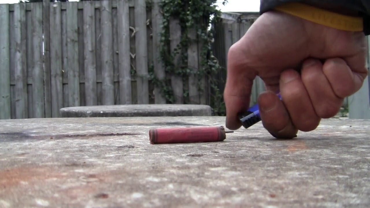 Een persoon gaat met een aansteker een vuurwerkrotje aansteken.