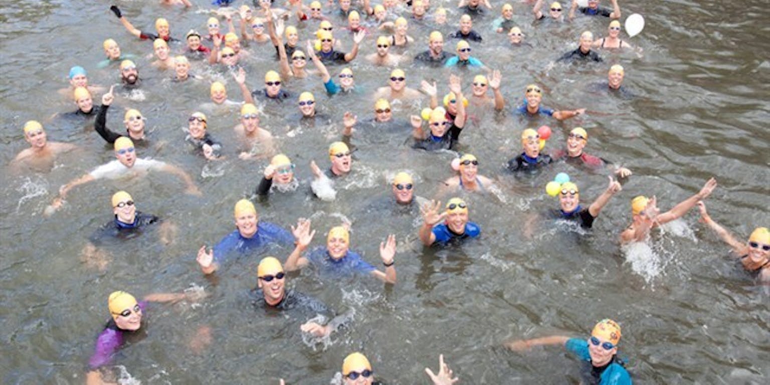 Een groep mensen die zwemmen in een gracht. Op de achtergrond is een rode ballon te zien.