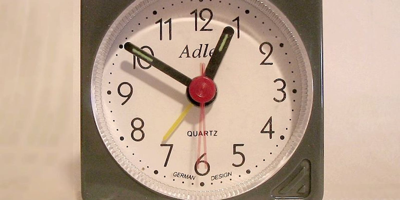 Een grijze wekker op een witte ondergrond.