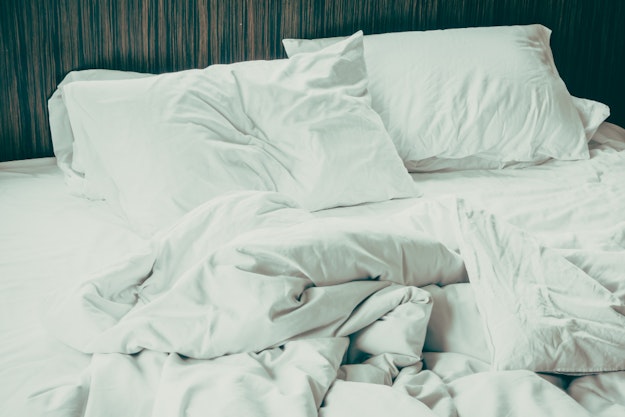 Leeg bed met witte lakens waar duidelijk in geslapen is.