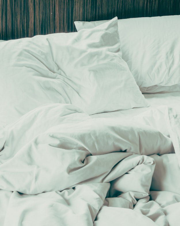 Leeg bed met witte lakens waar duidelijk in geslapen is.